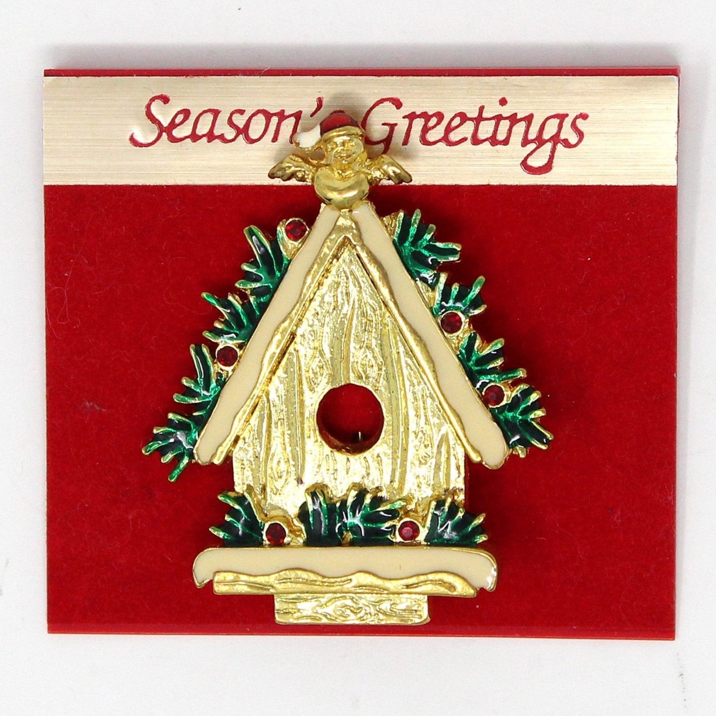 A vintage gold-tone metal brooch featuring a Christmas birdhouse with enamel details, rhinestones, and a small bird wearing a Santa hat.