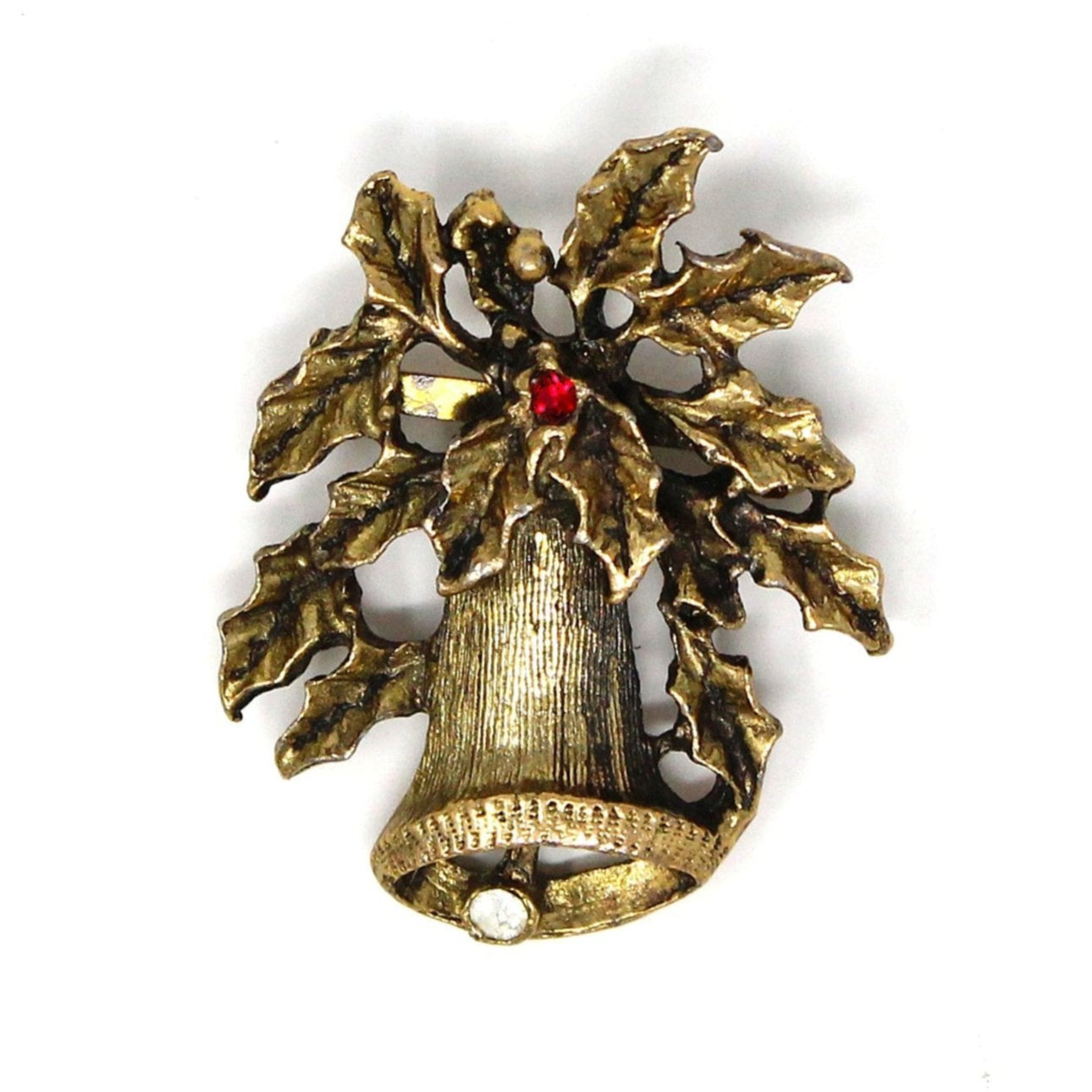 A vintage gold-tone metal brooch featuring a Christmas bell and holly leaves with red and white rhinestones.