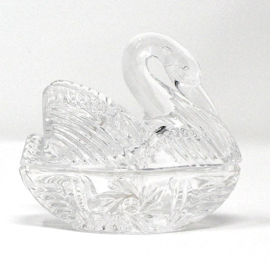 A vintage clear crystal trinket box designed in the shape of a swan lying in a nest.