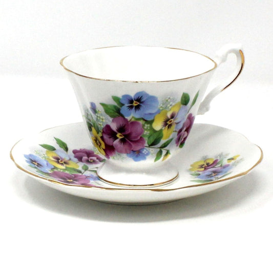 A vintage bone china teacup and saucer set with a floral pattern of multicolor violas/pansies and gold rims.