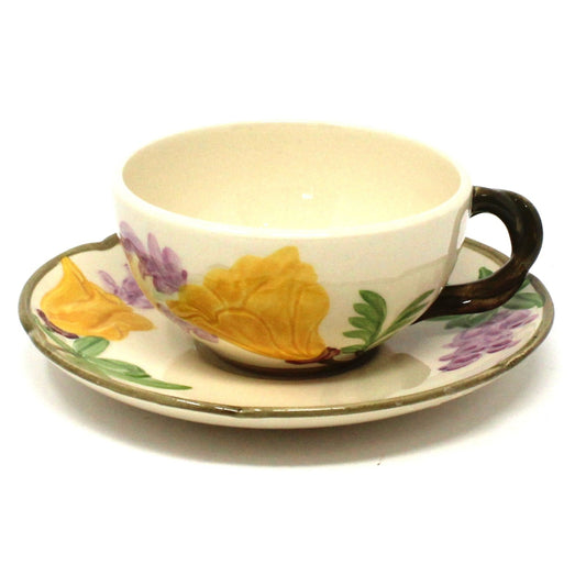 A vintage Franciscan teacup with embossed yellow and purple poppy flowers on the saucer, featuring a beige color and a dark brown handle.