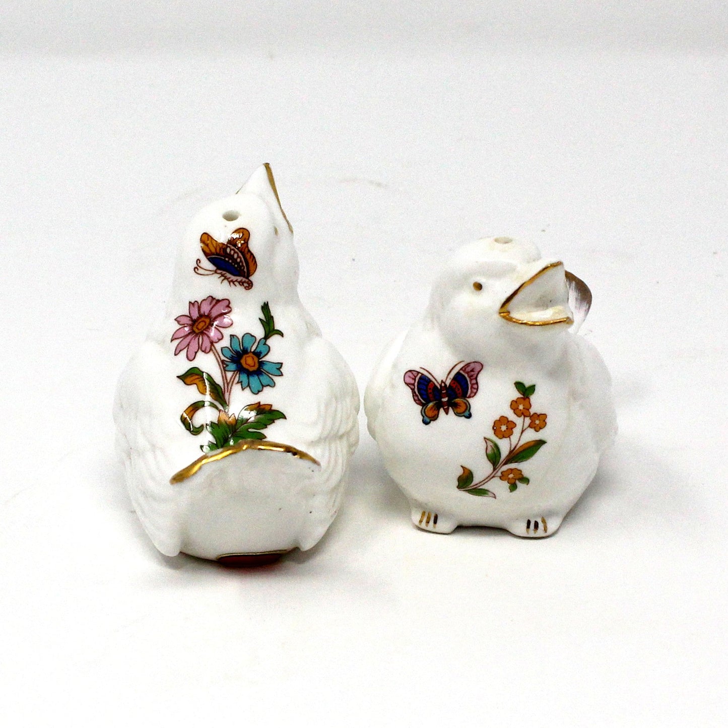 A pair of vintage white bone china salt and pepper shakers, featuring floral and butterfly designs with gold accents.