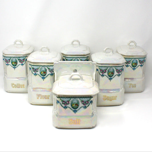A set of six antique Mepoco Ware porcelain canisters with blue and white floral patterns and gilded lettering, including lids.
