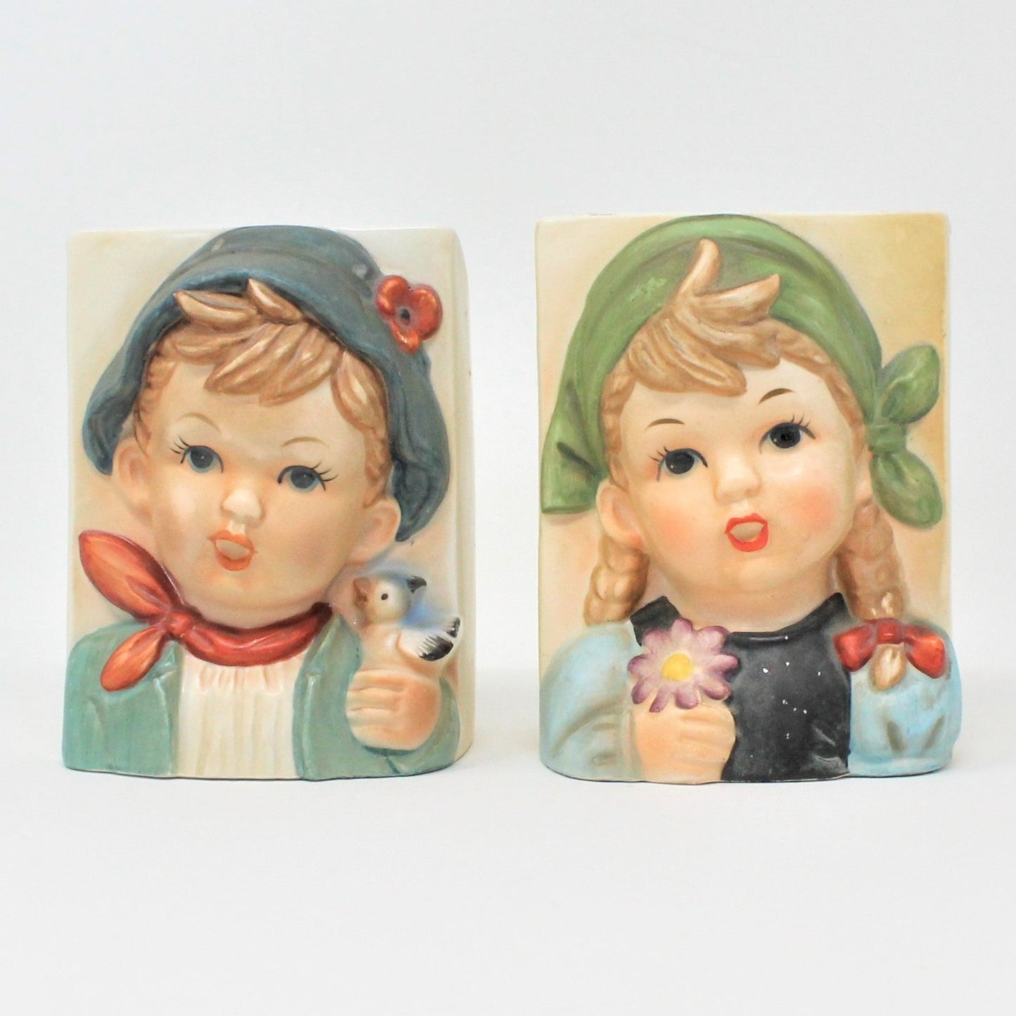 A pair of vintage ceramic planters featuring Hummel-like children, a boy and a girl, with the boy holding a bird and the girl a flower. Collectible pottery