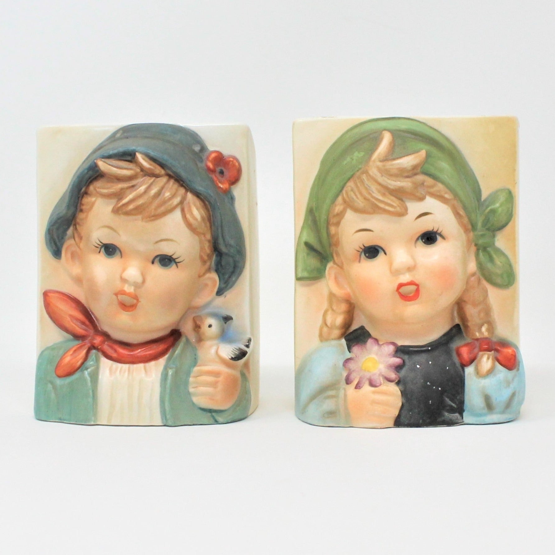 A pair of vintage ceramic planters featuring Hummel-like children, a boy and a girl, with the boy holding a bird and the girl a flower. Collectible pottery