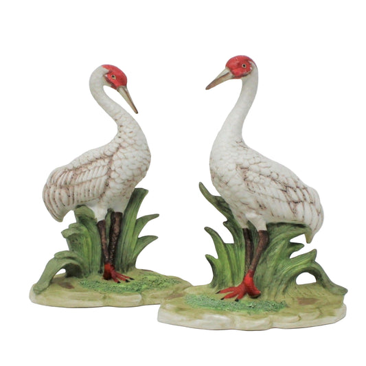 A pair of vintage Royal Crown / Arnart bisque porcelain figurines of red-crowned cranes standing on a green base