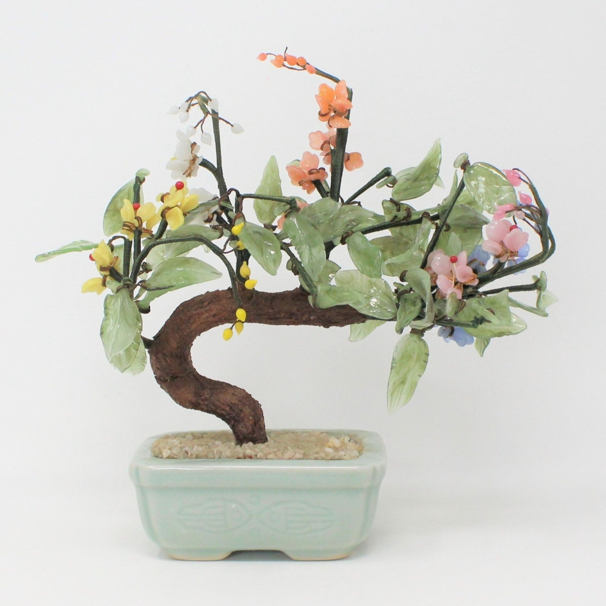 A jade glass bonsai tree with multicolor floral decorations placed in a celadon ceramic planter.