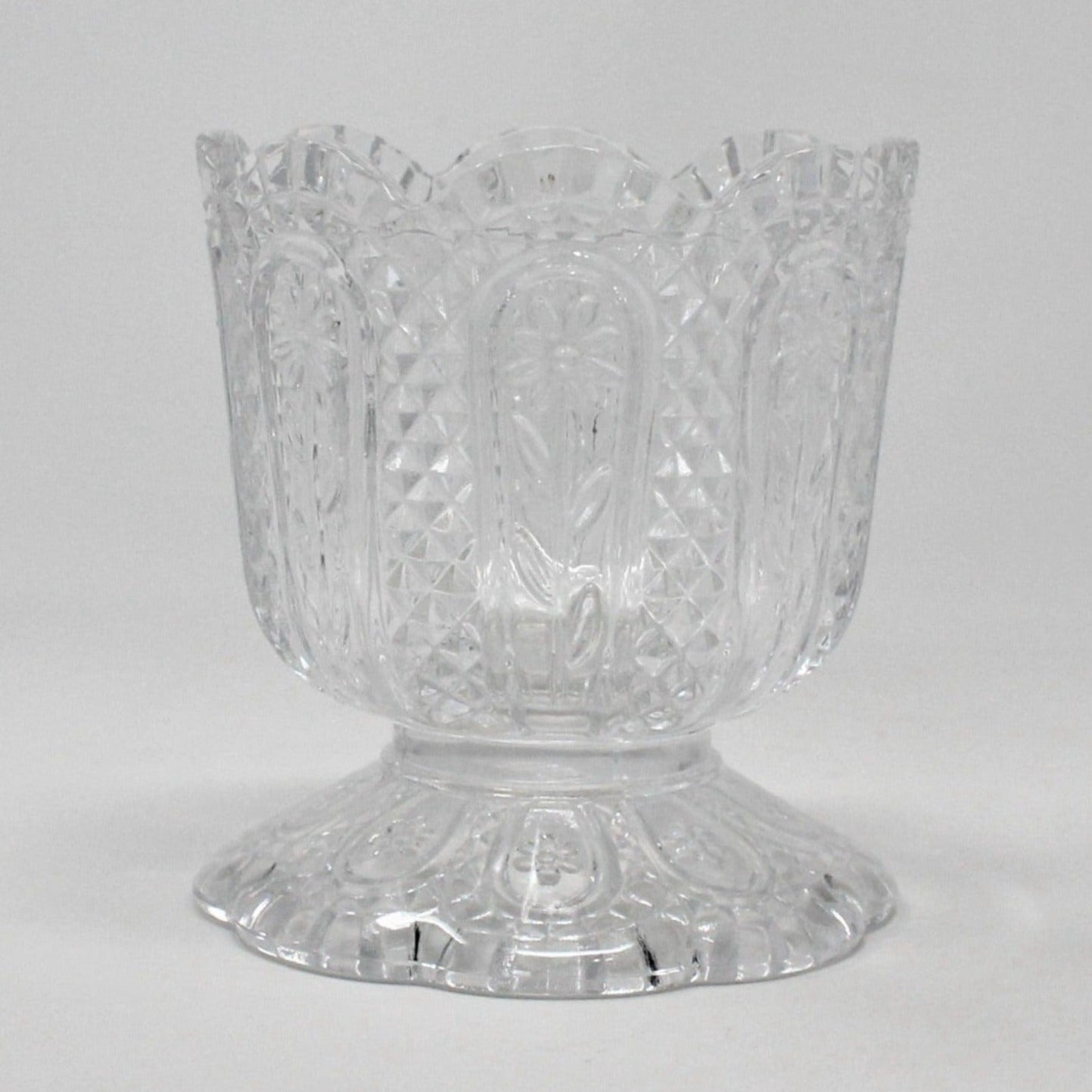 A vintage Fostoria clear glass candle holder with a Daisy and Diamond pattern, featuring a footed base and a pedestal base, with the brand name 'AVON' embossed on the bottom.