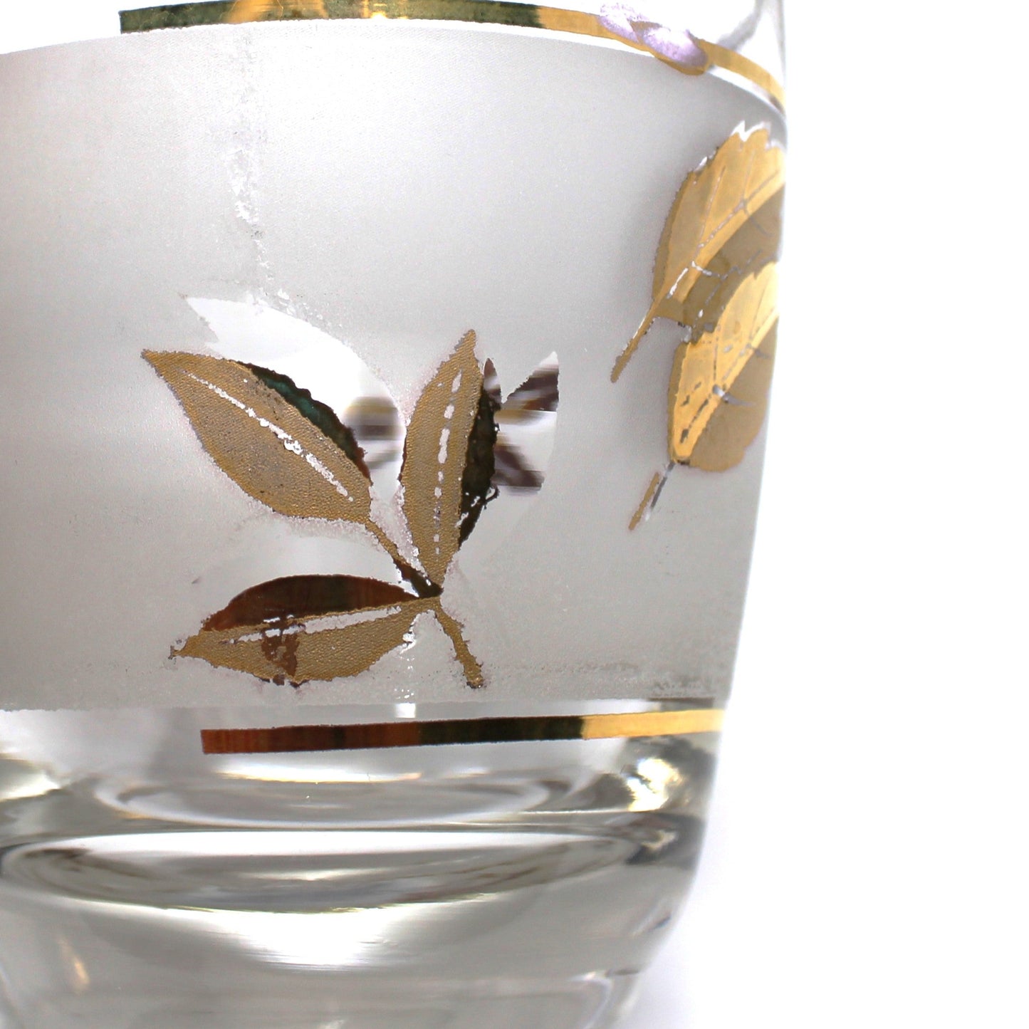 Hand holding a glass with gold leaf design on a white surface with more glasses in the background.