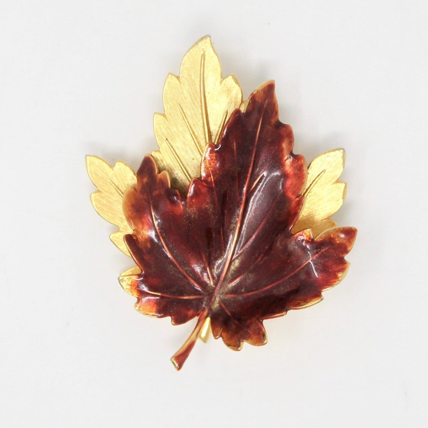 A vintage gold-tone brooch shaped like a pair of maple leaves with enamel detailing.