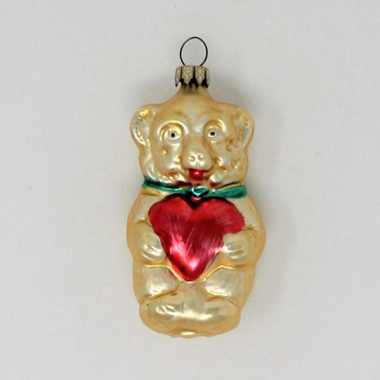 A vintage Germany glass Christmas ornament featuring a gold-colored teddy bear with a red heart-shaped detail.
