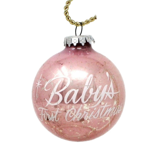 A vintage pink mercury glass ball Christmas ornament with white enamel text 'Baby's First Christmas' and starburst designs, with a silver metal cap.