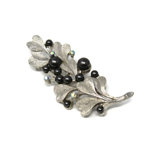 Silver brooch with leaves and black beads on a white background
