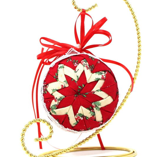 A vintage quilted fabric ornament with an eight-pointed star design, featuring red and green fabric, lace, and a red ribbon on top as hanging loop.