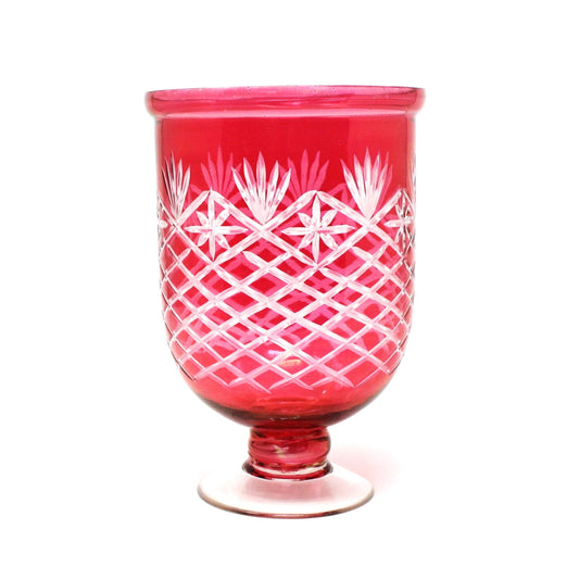 A vibrant ruby red cut glass vase with clear feet, featuring a geometric pattern of cuts like starbursts and fans.