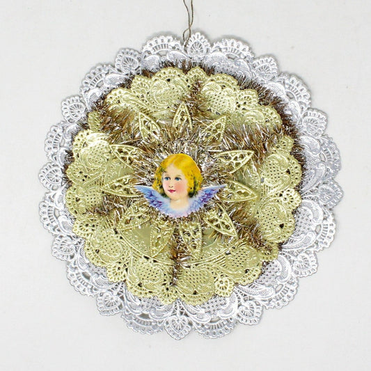 A vintage Christmas ornament featuring a die-cut foil medallion with a tinsel and a gold foil star, centered around a blond angel with purple wings.