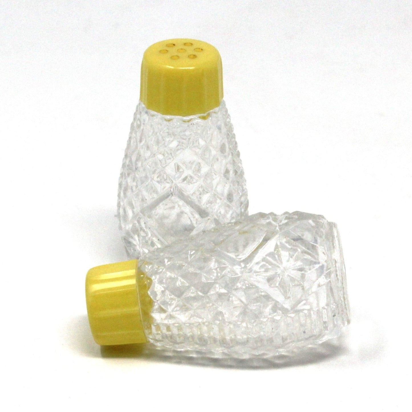 A pair of vintage salt and pepper shakers with a clear glass body and yellow bakelite tops, featuring embossed patterns and measurements on the base.