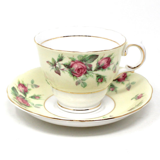 A vintage bone china teacup with pink roses and a light yellow band, featuring a matching saucer, both with gold rims.