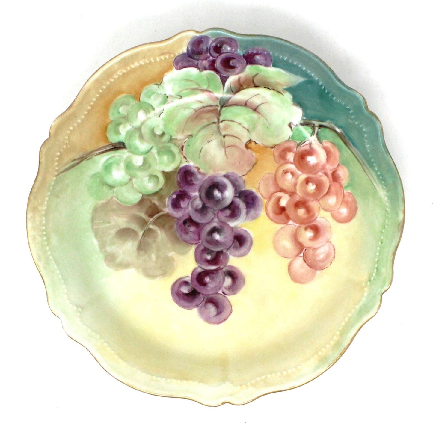 Antique shallow porcelain bowl with hand-painted grapes in purple, green, and red on a yellow and green background with a swirled rim. Royal Austria.