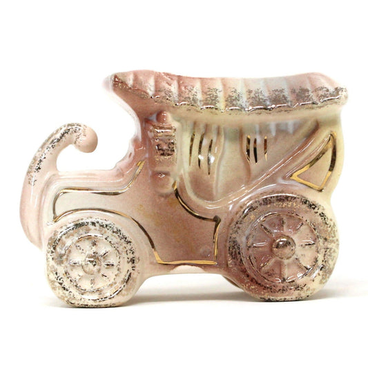 A vintage ceramic planter in the shape of an antique pink car with gold accents, featuring window side curtains.