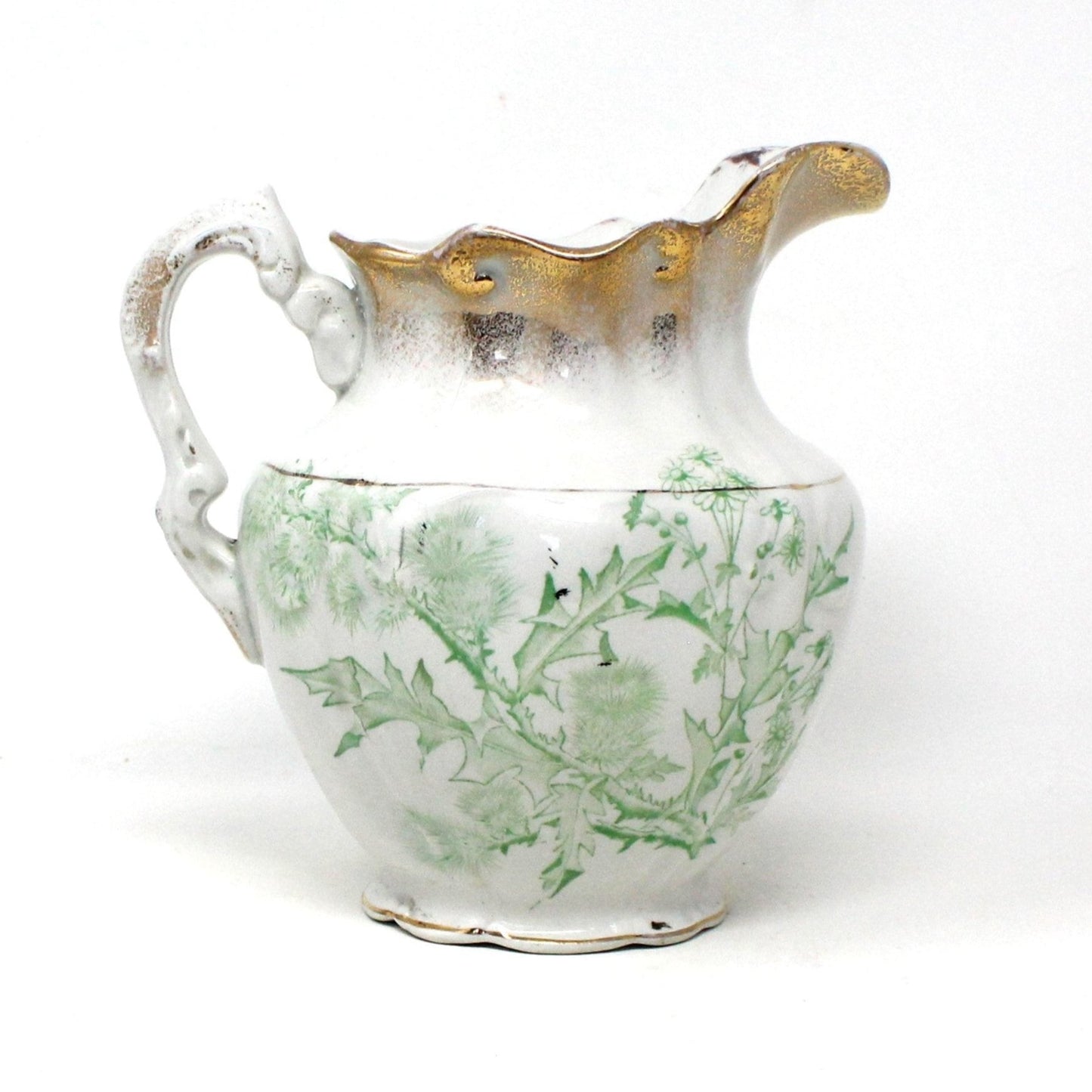 Antique white earthenware pitcher with green thistle leaf patterns and brushed gold details on the rim.