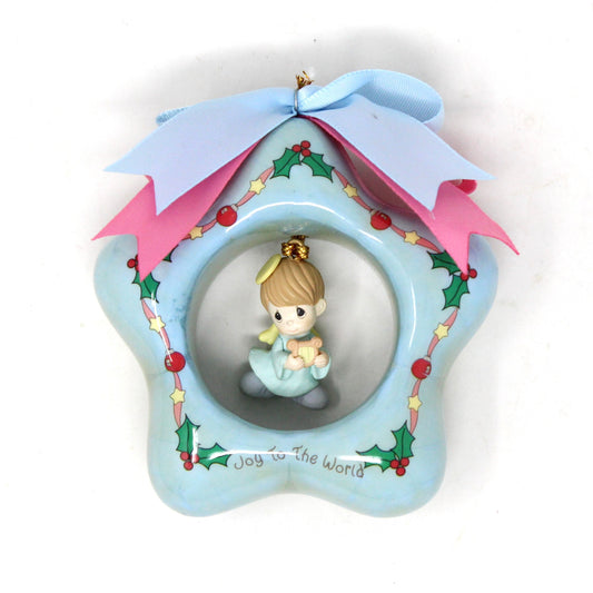Vintage Precious Moments ornament featuring a star shape with a dangle angel charm figurine in the center, adorned with blue, holly, pink ribbon, and stars, with a pink and blue satin ribbon on top.
