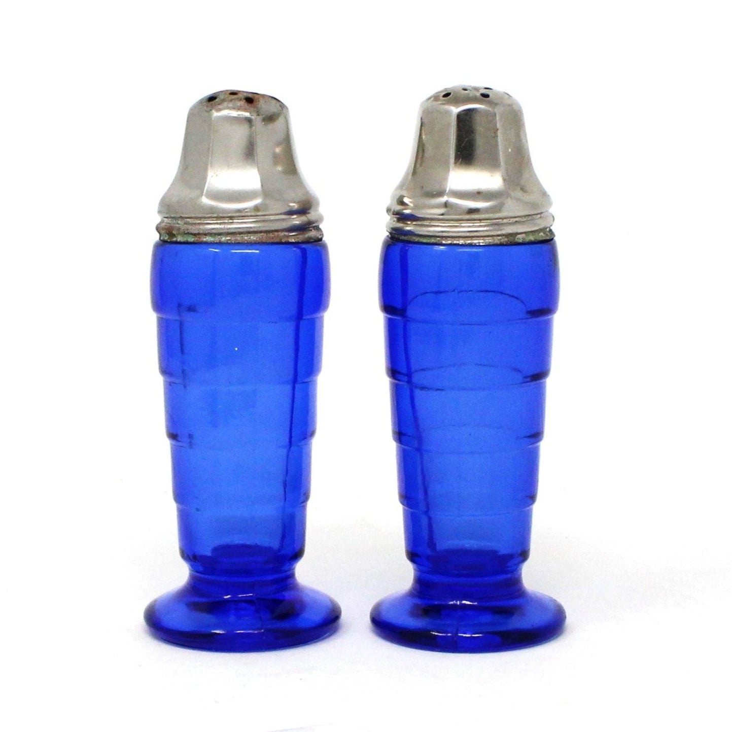 A pair of vintage cobalt blue glass salt and pepper shakers with metal lids, featuring the Moderntone pattern by Hazel Atlas.