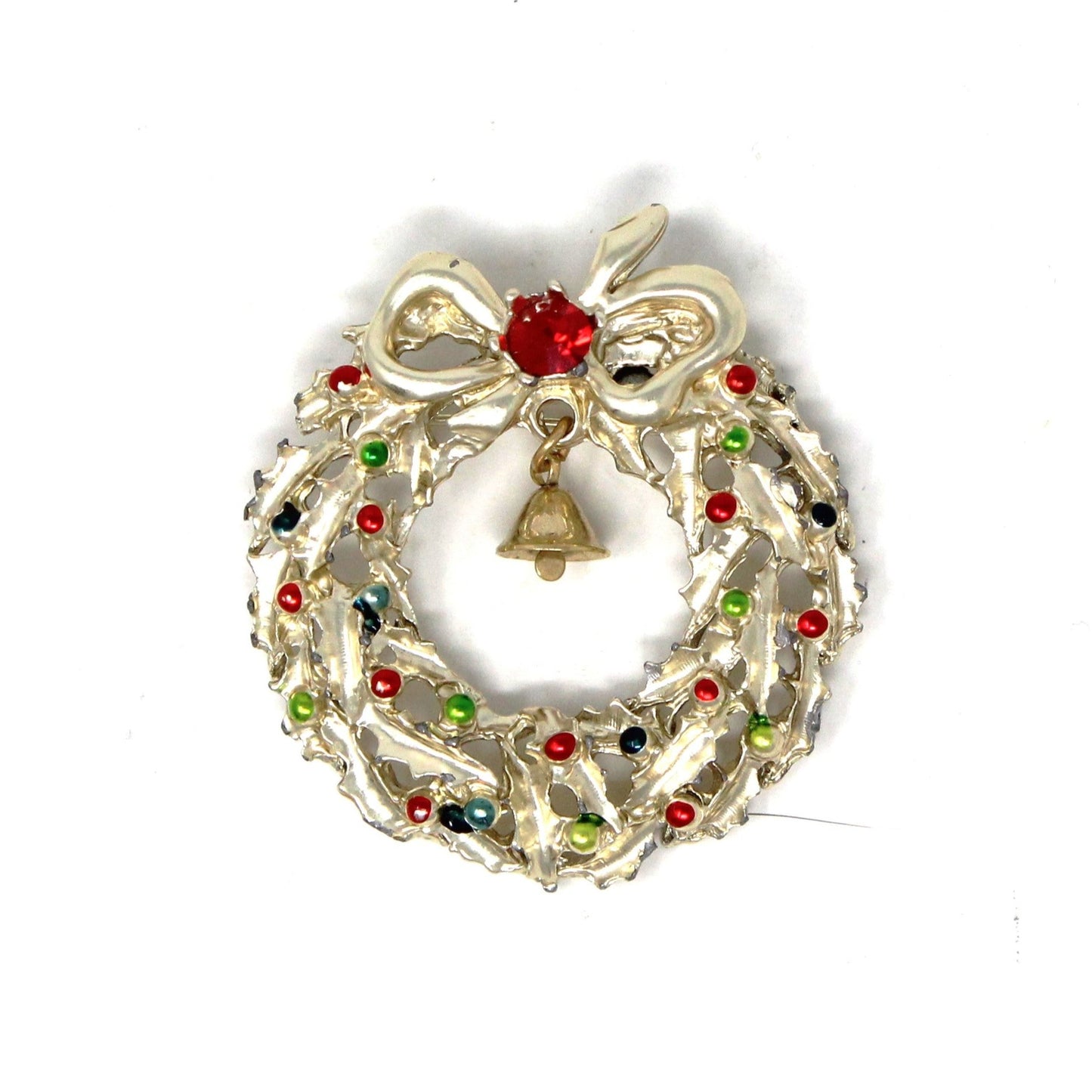 A vintage gold-tone metal brooch featuring a Christmas wreath with a dangle bell, red rhinestone, and enamel ornaments in red, green, and blue.