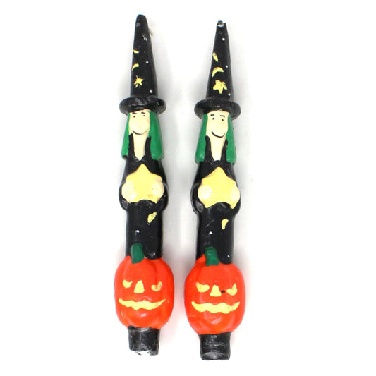 A pair of vintage taper candles featuring a Halloween figural witch & pumpkin design with a black hat adorned with stars and a green hairdo, standing on an orange pumpkin. The candles are unused and have a black base.