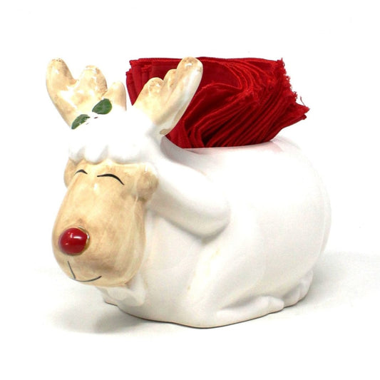 A ceramic napkin holder shaped like a Christmas moose with a stack of red cloth cocktail napkins on its back.