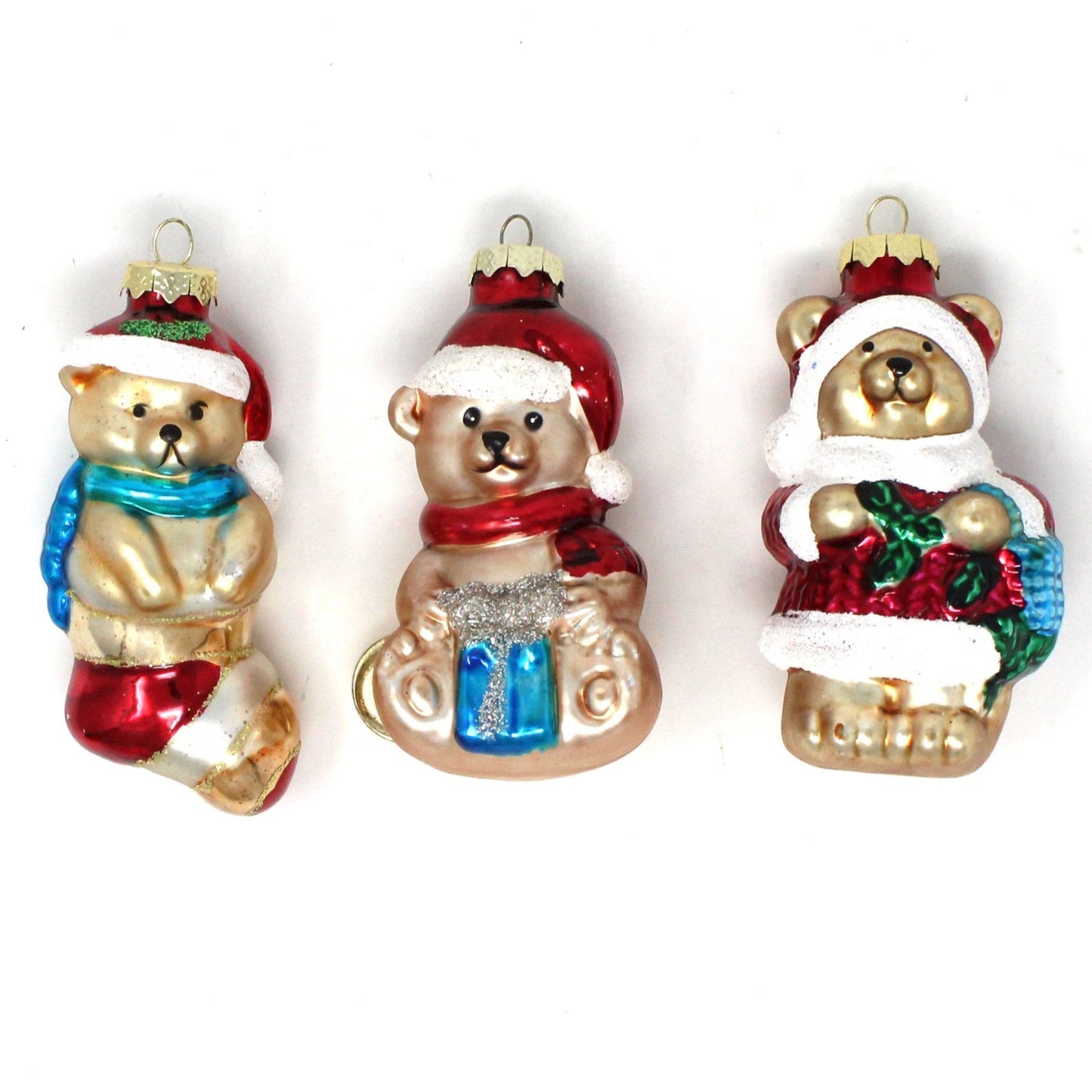 Set of three vintage glittered blown glass teddy bear ornaments with Santa hats, each holding a different items: one with a blue and silver glitter gift box, one with a red and green holly, and one with a red and white Christmas stocking.