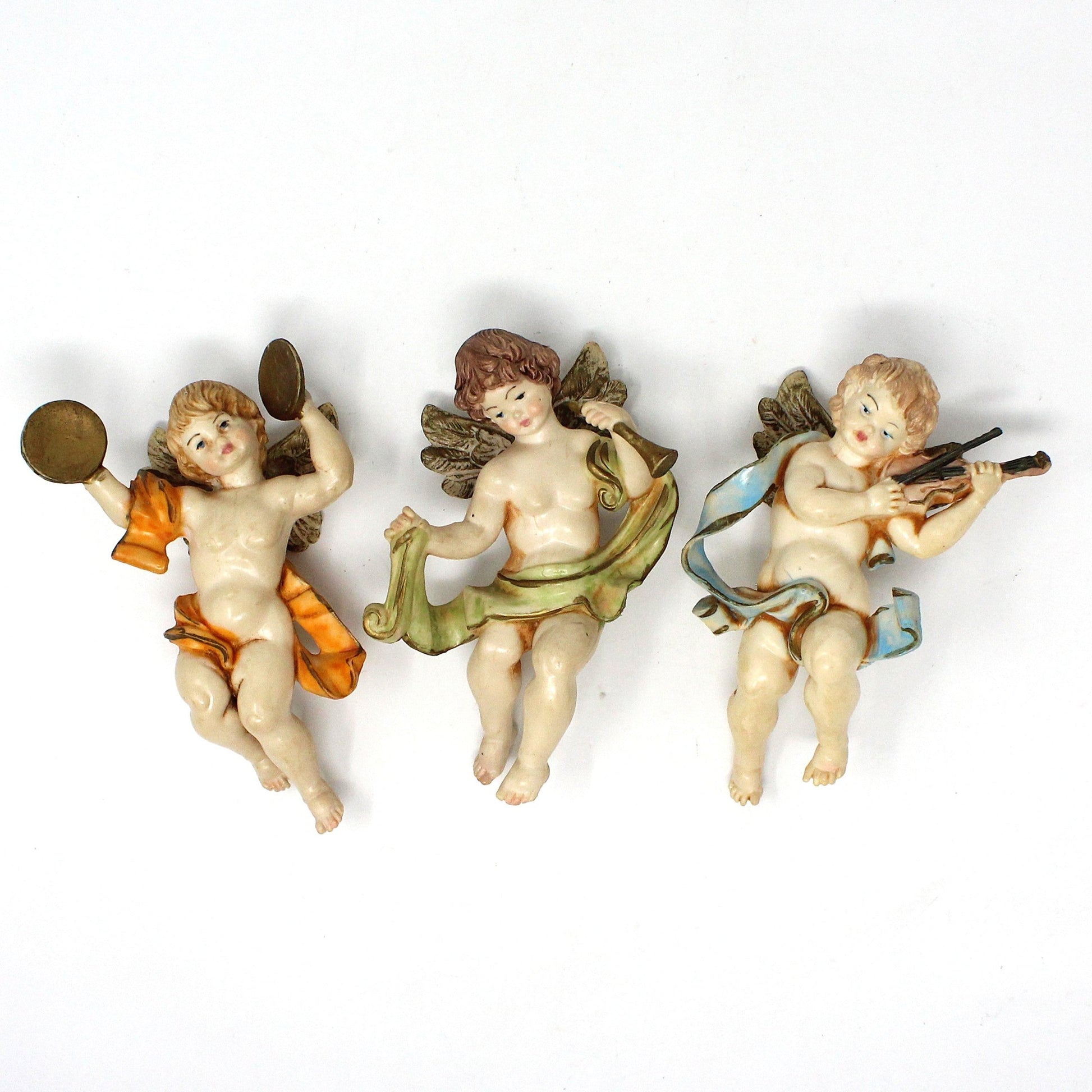 Set of three vintage Christmas ornaments featuring cherub angels playing musical instruments. Each ornament is painted with different colors, representing different musical instruments.  1980's