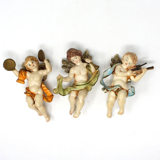Set of three vintage Christmas ornaments featuring cherub angels playing musical instruments. Each ornament is painted with different colors, representing different musical instruments.  1980's