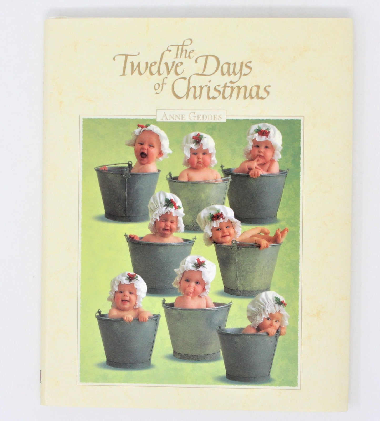 The cover of the book 'The Twelve Days of Christmas' by Anne Geddes features multiple photographs of babies in Christmas-themed settings, such as in a bucket and with a Christmas tree, with a dust jacket.