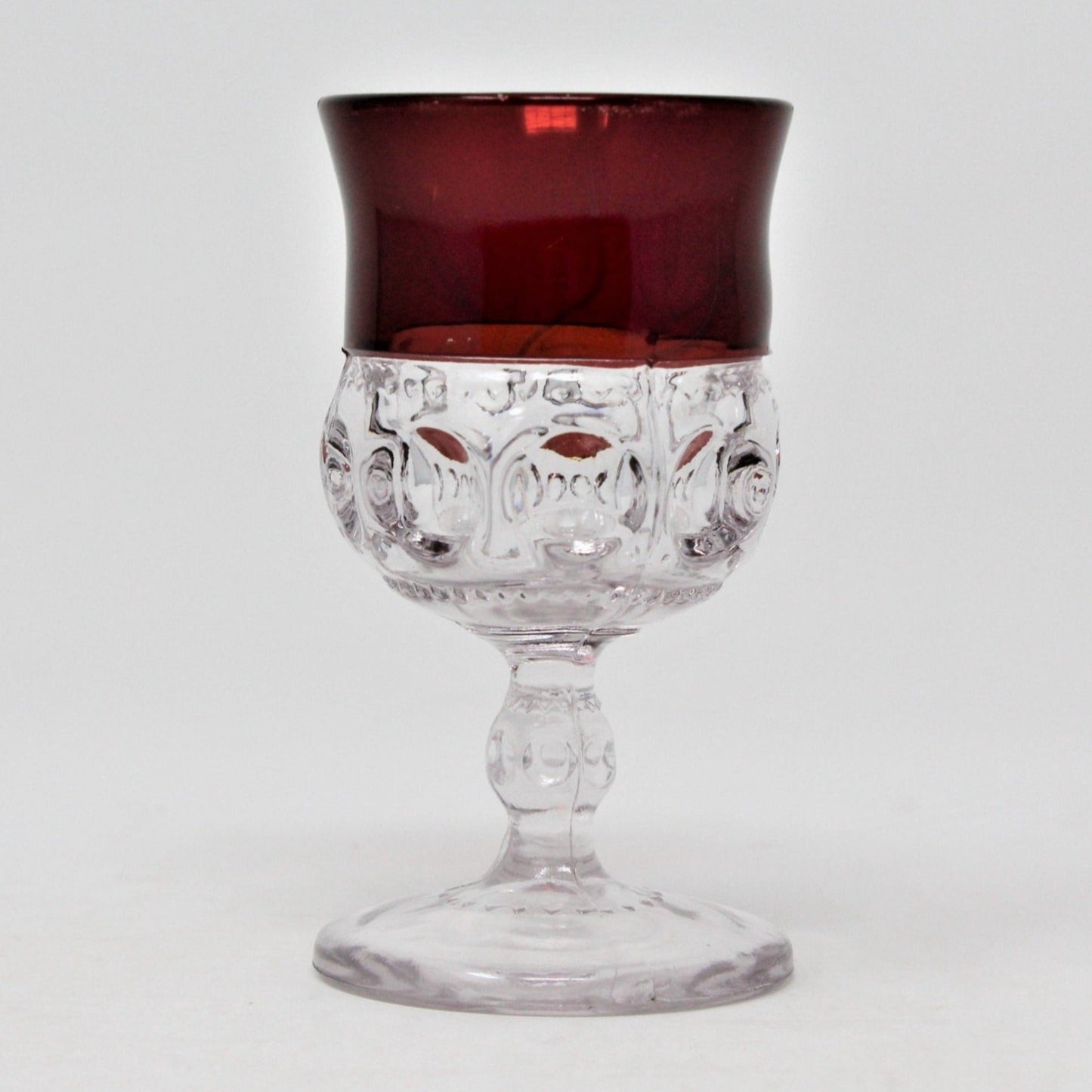 An antique clear glass cordial from Adams Glass. Red flashing on top and traditional oval and zigzag markings of the Kings Crown pattern.