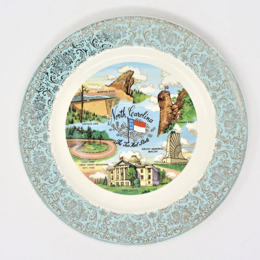 A vintage North Carolina State Plate.  Decorative ceramic plate with a blue border featuring gold floral filigree, and a central section depicting a map of North Carolina with landmarks. Mid Century souvenir