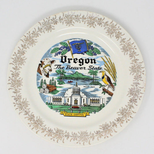 A vintage decorative Oregon state plate.  Ceramic plate featuring a gold filigree border, a depiction of an Oregon state flag, a beaver, and various landmarks related to the state of Oregon.