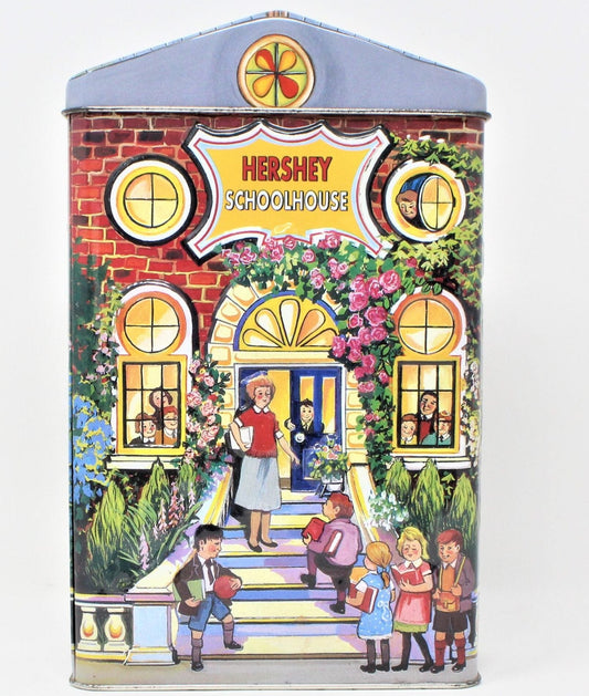 A collectible tin shaped like a school house with a colorful illustration of a teacher and children on the front, labeled Hershey's Village Series Canister #2 School House, 2000.