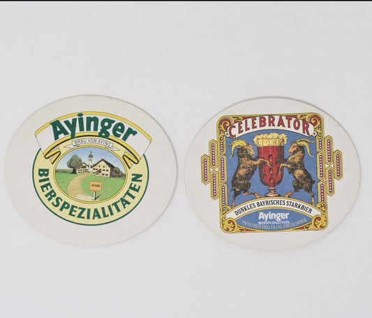Two oval Ayinger beer coasters, one with 'Ayinger Bierspezialitäten' logo and the other with 'Celebrator' beer label, both featuring German text and imagery related to the brand.