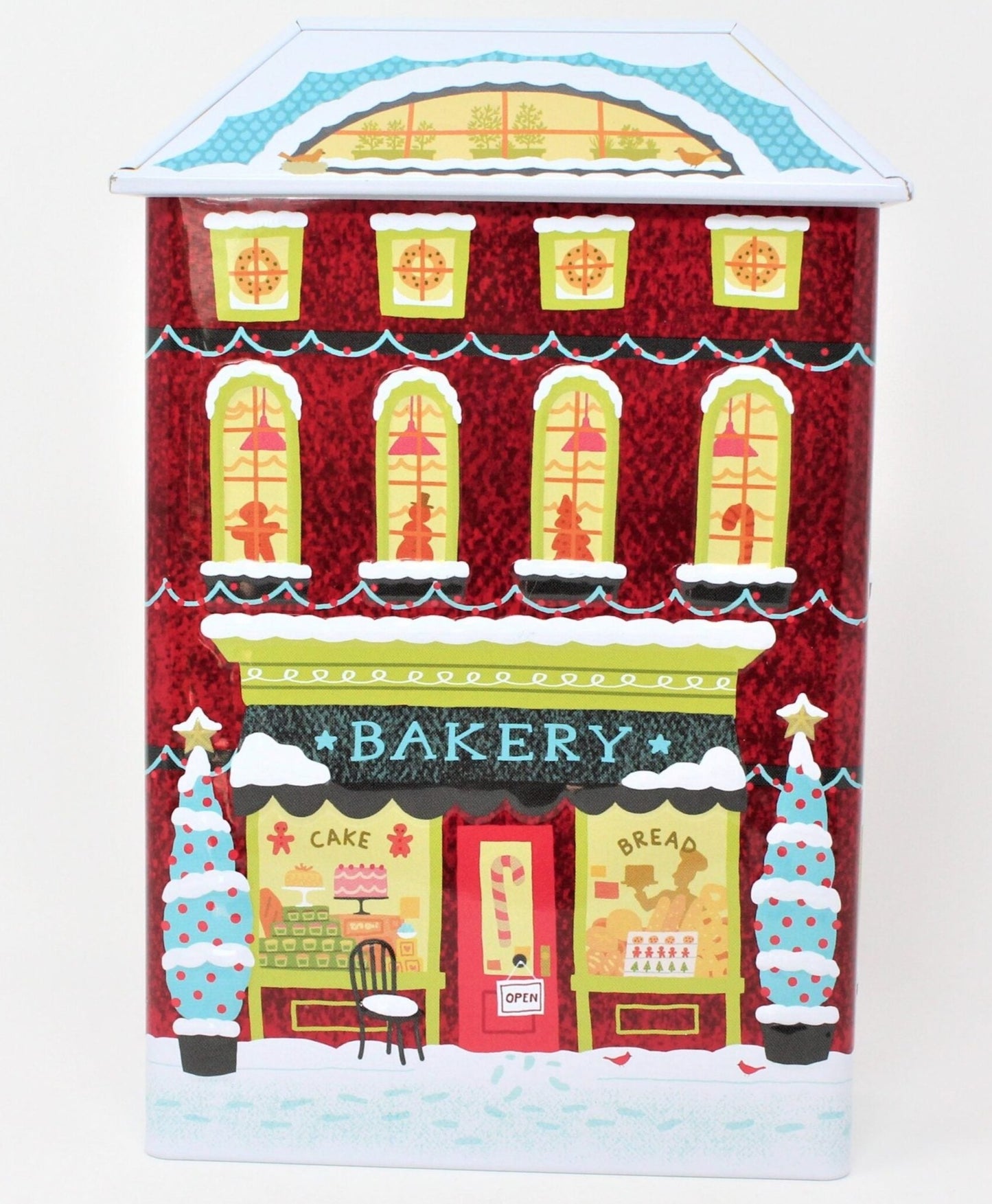 A collectible Christmas-themed cookie tin shaped like a red brick apartment building with a bakery shop on the bottom floor, decorated with festive designs and people engaging in holiday activities.