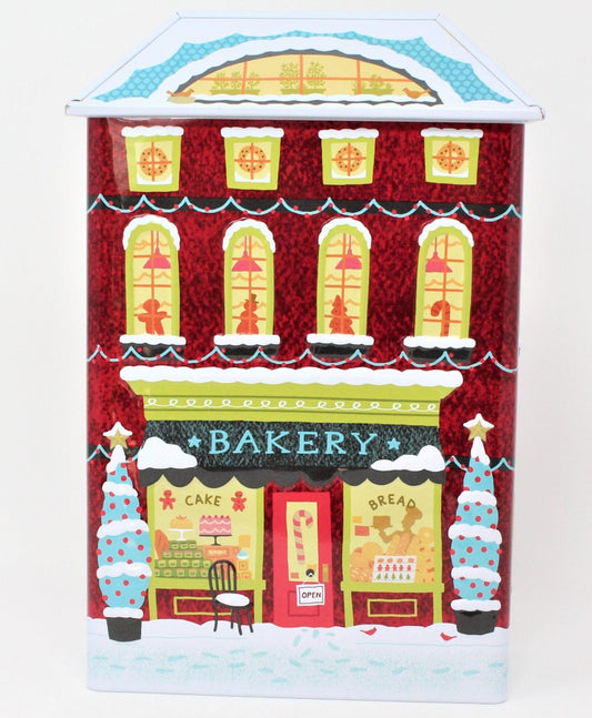 A collectible Christmas-themed cookie tin shaped like a red brick apartment building with a bakery shop on the bottom floor, decorated with festive designs and people engaging in holiday activities.