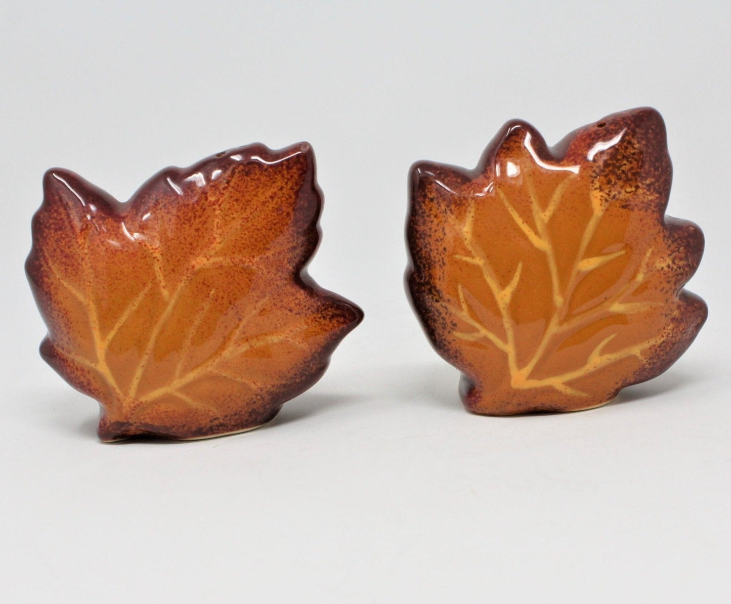 A pair of brown ceramic salt and pepper shakers designed to resemble leafs, with a speckled pattern and original stoppers.