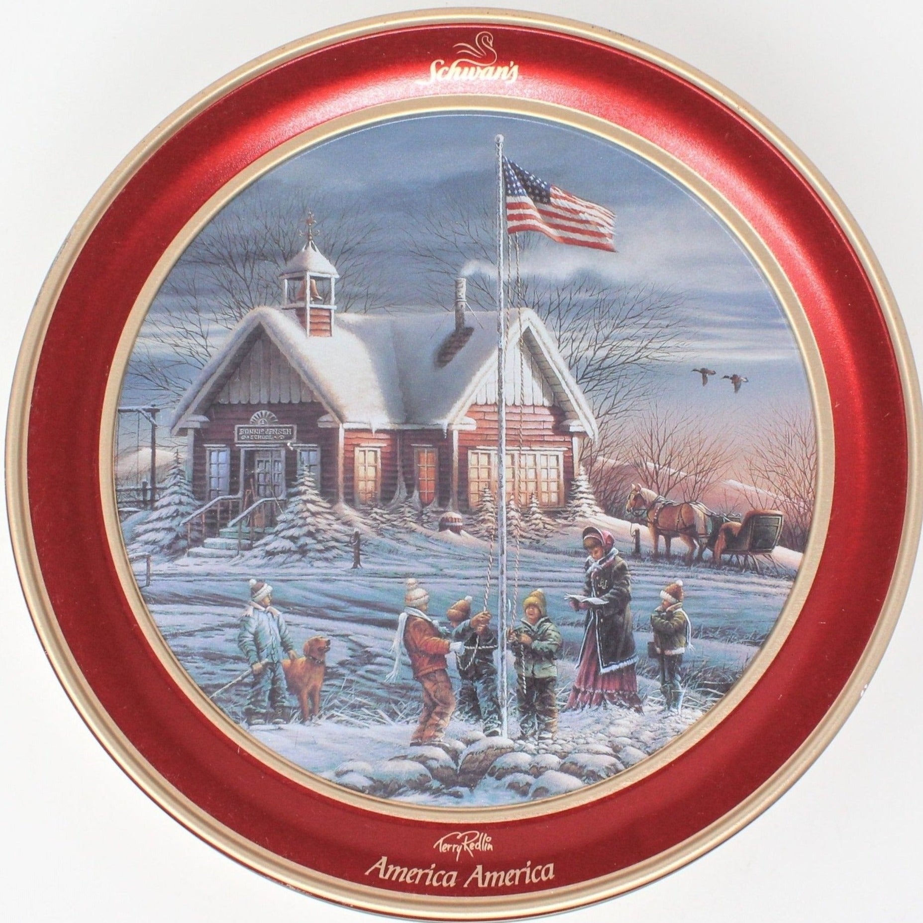 A round collectible tin with a painting of a snowy winter scene featuring a small school house, a teacher, and children. The tin has a red and gold color scheme with the 'Schwan's America America' text and flag motifs.
