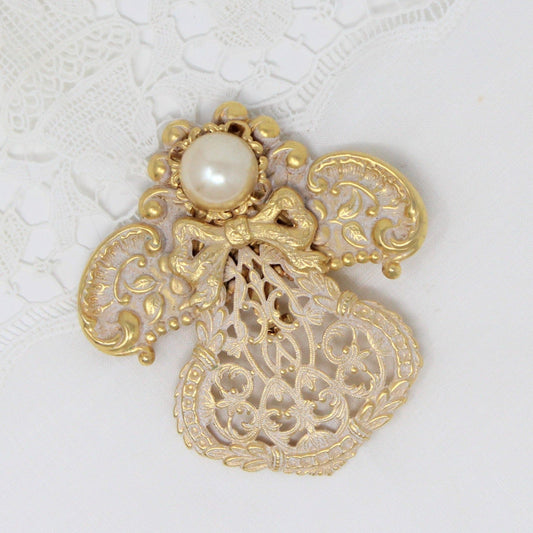 A vintage gold-tone metal brooch shaped like an angel, with white enamel filigree and a faux pearl, signed by Jane Davis.
