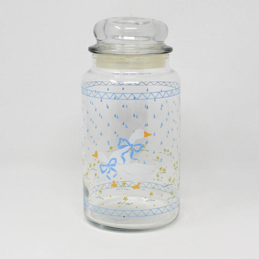 A clear glass apothecary jar with a vintage design featuring white geese with blue bows and raindrops, bordered with a blue triangle pattern on the top and bottom.