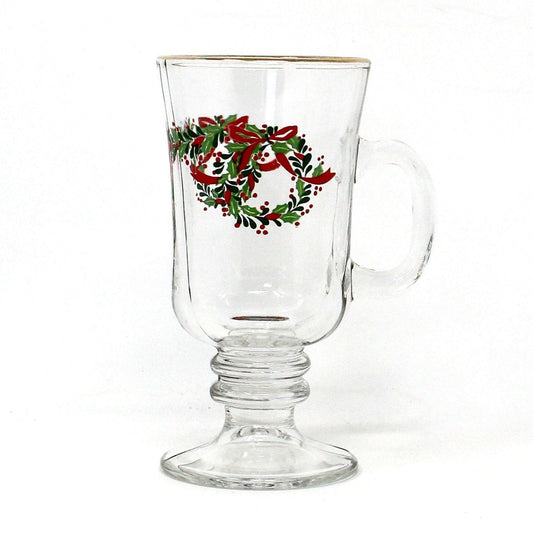 A clear glass Irish coffee mug with a Christmas wreath and holly design, featuring a red ribbon and gold rim.