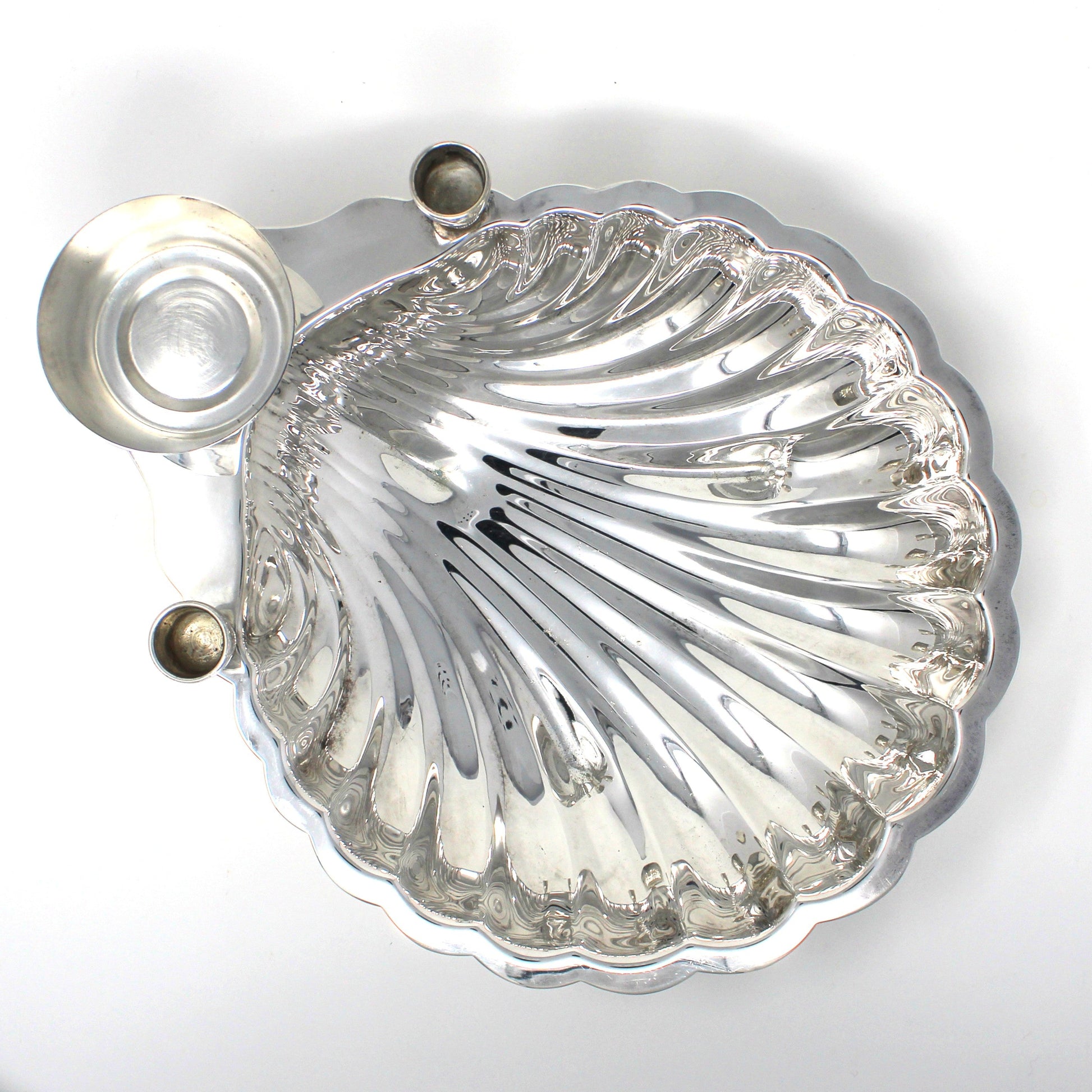 Top view of a silver shell-shaped serving dish with sauce bowl and candle holders.