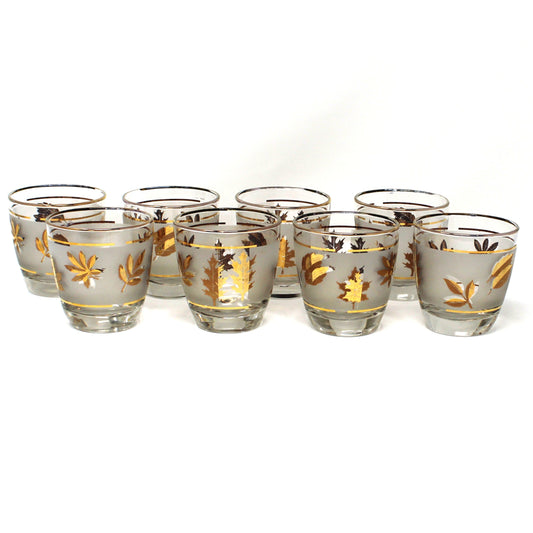 Set of eight small glass tumblers with gold leaf design on a white background
