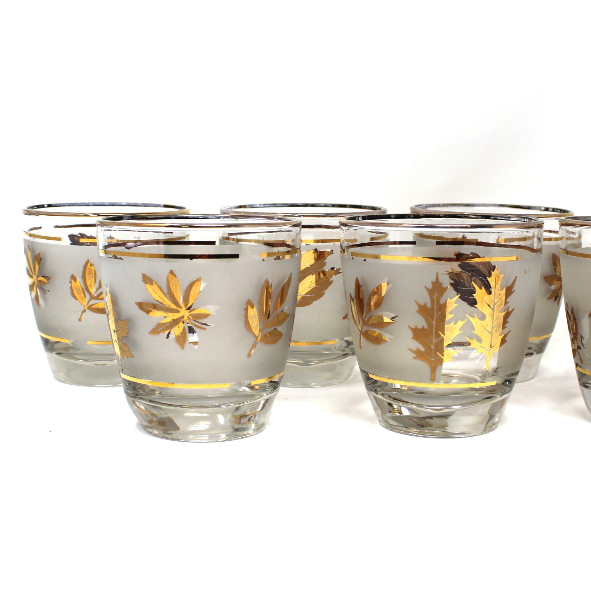 Set of eight glass shot glasses with gold leaf design on a white background