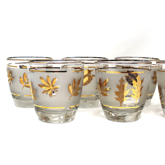Set of eight glass shot glasses with gold leaf design on a white background